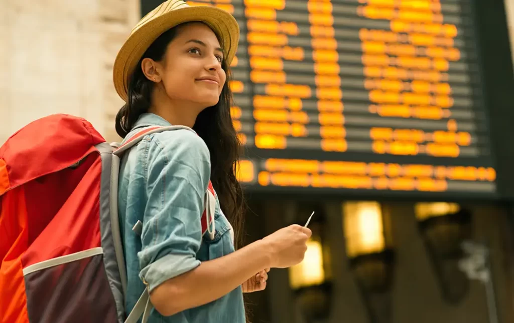 Young woman with a backpack traveling through Europe with her Travel Authorization at a train station.