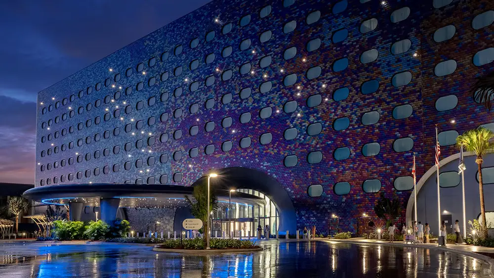 a Modern Hotel Building with a Curved Entrance, Rows of Oval Windows, and a Colorful, Mosaic-like Exterior, Illuminated at Night with Reflections on the Wet Pavement and Palm Trees Nearby. - Favorite Grampy Travels - Favorite Grampy Travels 2026