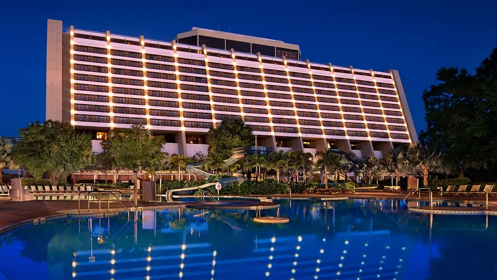 a Large, Modern Hotel—bay Lake Tower—stands Behind a Swimming Pool Surrounded by Lounge Chairs and Palm Trees at Night, Its Illuminated Balconies Shining. the Building Reflects on the Calm, Blue Water—a Perfect Scene for Magic Kingdom Resorts Fans. - Favorite Grampy Travels