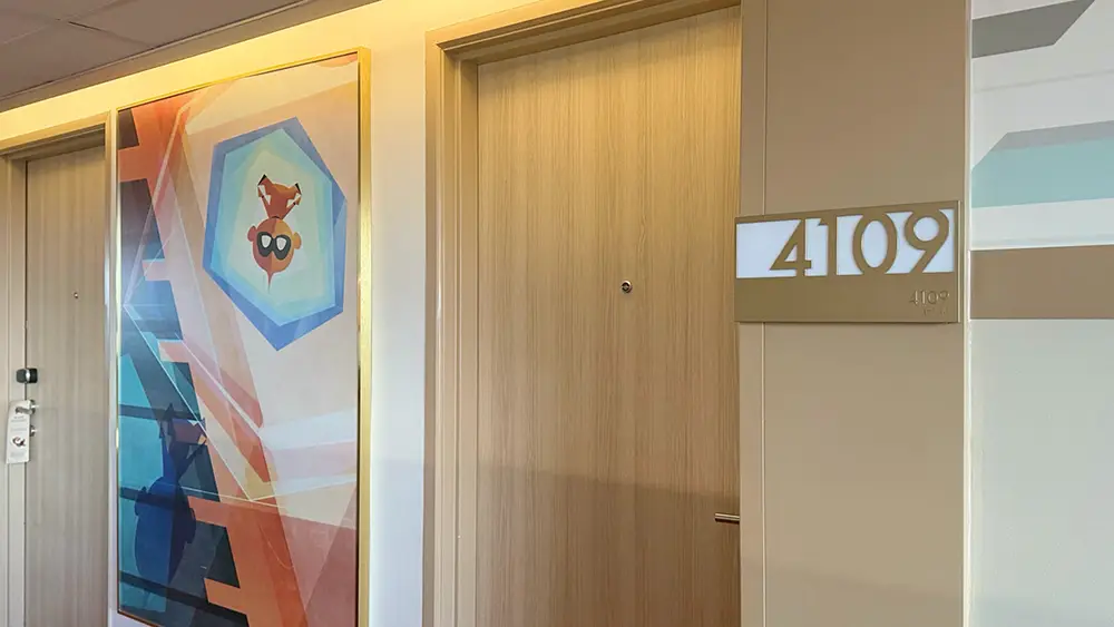 a Hallway in Bay Lake Tower Features Light Wood Doors, Room Number 4109 on a Wall Plaque, and an Abstract Colorful Painting with Geometric Shapes and a Stylized Face with Glasses, Reflecting Disney's Contemporary Resort style. - Favorite Grampy Travels