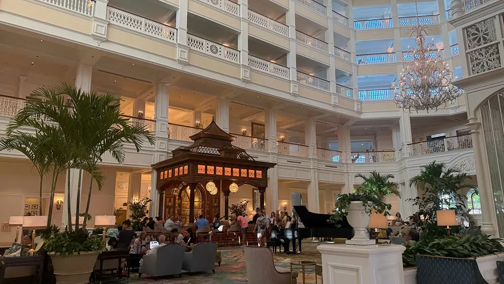 Spacious Hotel Lobby with High Ceilings, White Railings, a Grand Piano, Indoor Plants, and a Wooden Kiosk-style Structure with Clocks. Multiple Floors Are Visible—an Elegant Scene Inside Disney's Grand Floridian Resort. - Favorite Grampy Travels