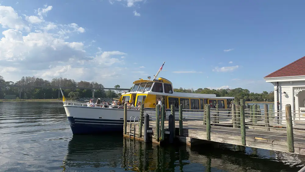 a Yellow and White Passenger Boat is Docked at a Wooden Pier on a Calm Lake Near Disney's Grand Floridian Resort, with people seated on the boat and a partly cloudy blue sky in the background—a perfect Family Guide moment. - Favorite Grampy Travels