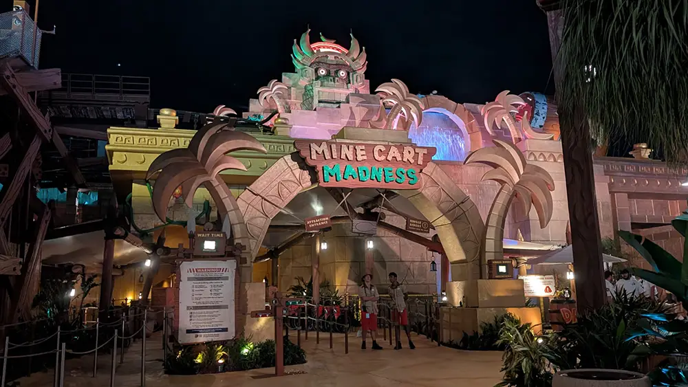 a Colorful, Temple-themed Amusement Park Ride Entrance at Night Named Mine Cart Madness, with Palm-like Decorations, Glowing Lights, and Two Staff Members Standing by the Entry—it Feels Like a Scene from a Family Movie and is Truly Worth Seeing. - Favorite Grampy Travels