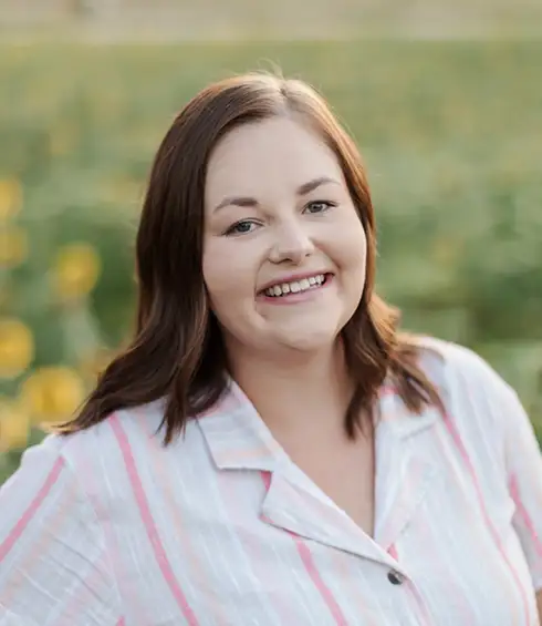 Samantha Malone, Travel Agent with Favorite Grampy Travels, is Shown with Shoulder-length Brown Hair, Wears a Light-colored Shirt with Pink Stripes and Smiles Outdoors, a Blurred Green Field in the Background. - Favorite Grampy Travels - Favorite Grampy Travels 2026