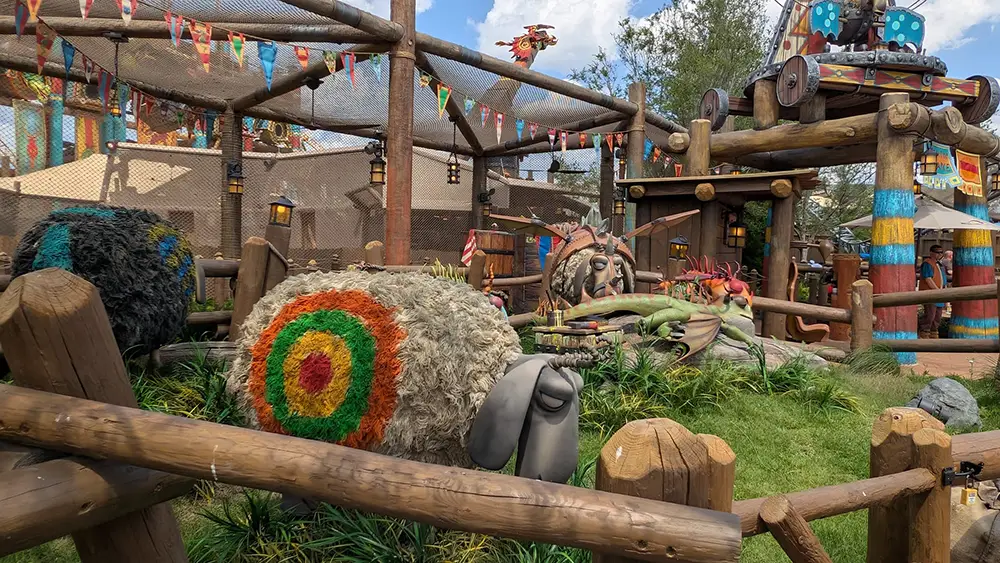 a Theme Park Scene at Universal Studios Features a Large, Whimsical Sheep Statue with a Colorful Target Painted on Its Side, Surrounded by Wooden Fences, Playful Decorations, and Cartoon-style Props. Blue Sky and Trees Are Visible in the Background. - Favorite Grampy Travels - Favorite Grampy Travels 2026