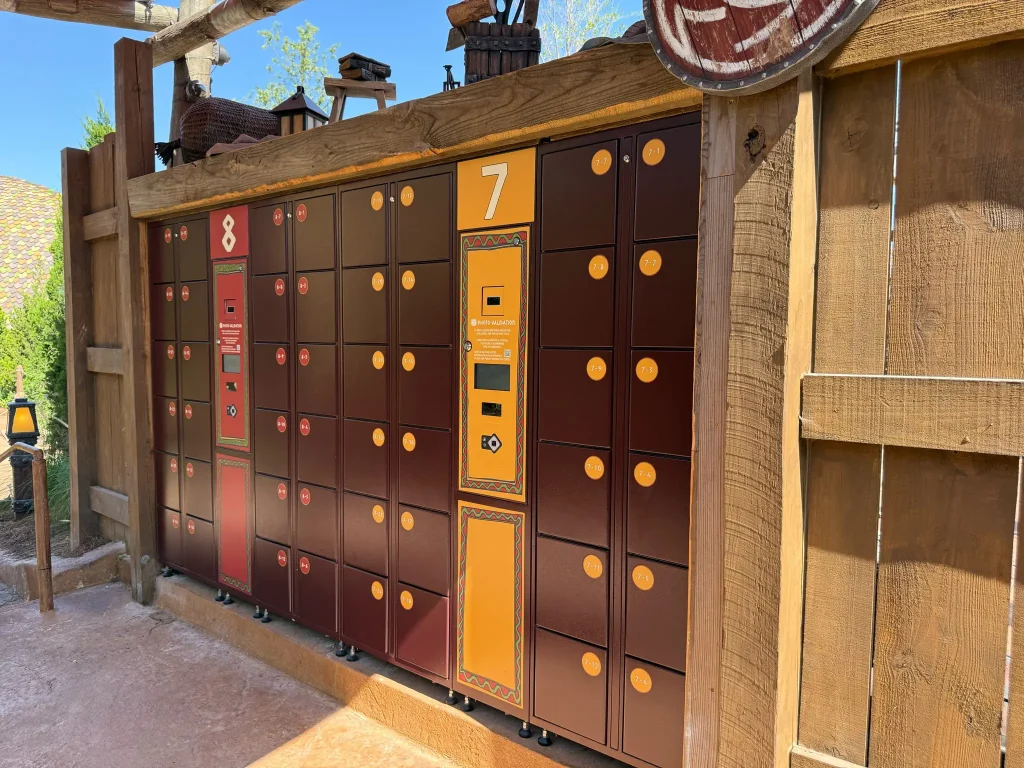 A set of Universal Orlando Locker units with brown and orange doors, labeled 7 and 8, is mounted against a wooden fence in a sunny area—perfect for storing your belongings during your Epic Universe adventure. - Favorite Grampy Travels