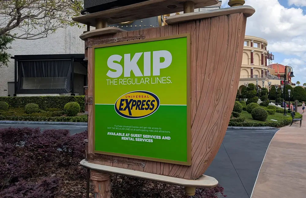 a Sign at Universal Studios Reads Skip the Regular Lines. Universal Express Pass—available at Guest Services and Rental Services—lets You Enjoy Rides Like Hagrid - Favorite Grampy Travels 2026's Magical Creature Motorbike Adventure faster against a green and yellow background. - Favorite Grampy Travels