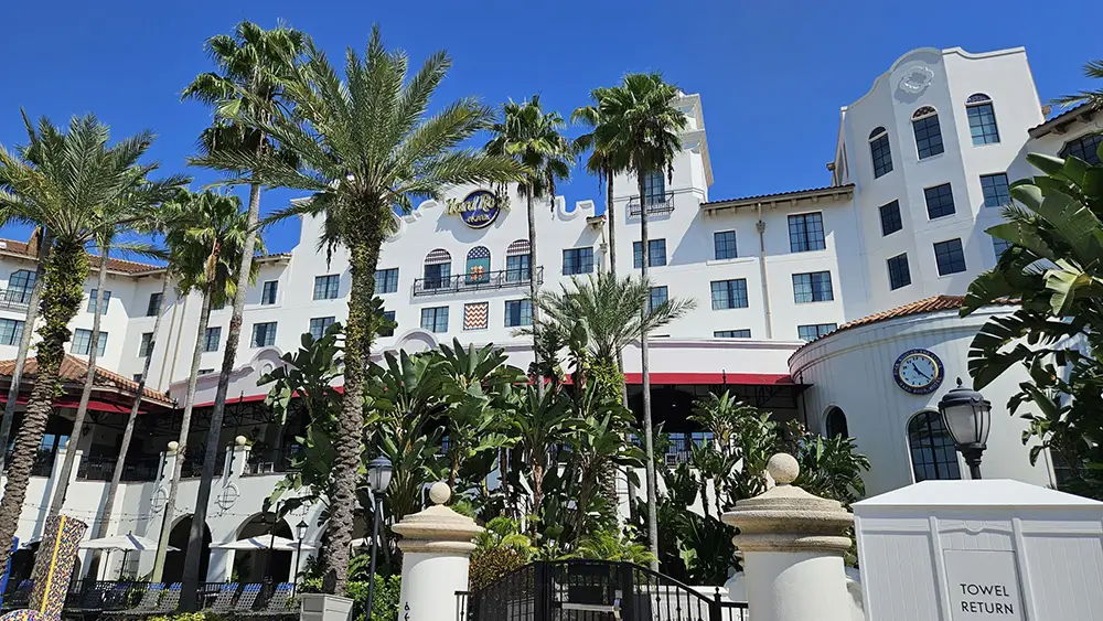 a White, Multi-story Hotel with Spanish-style Architecture Welcomes Guests Near Universal Orlando Resort, Surrounded by Palm Trees and Lush Greenery. a Towel Return Sign is Visible Near the Entrance Under a Bright Blue Sky. - Favorite Grampy Travels - Favorite Grampy Travels 2026