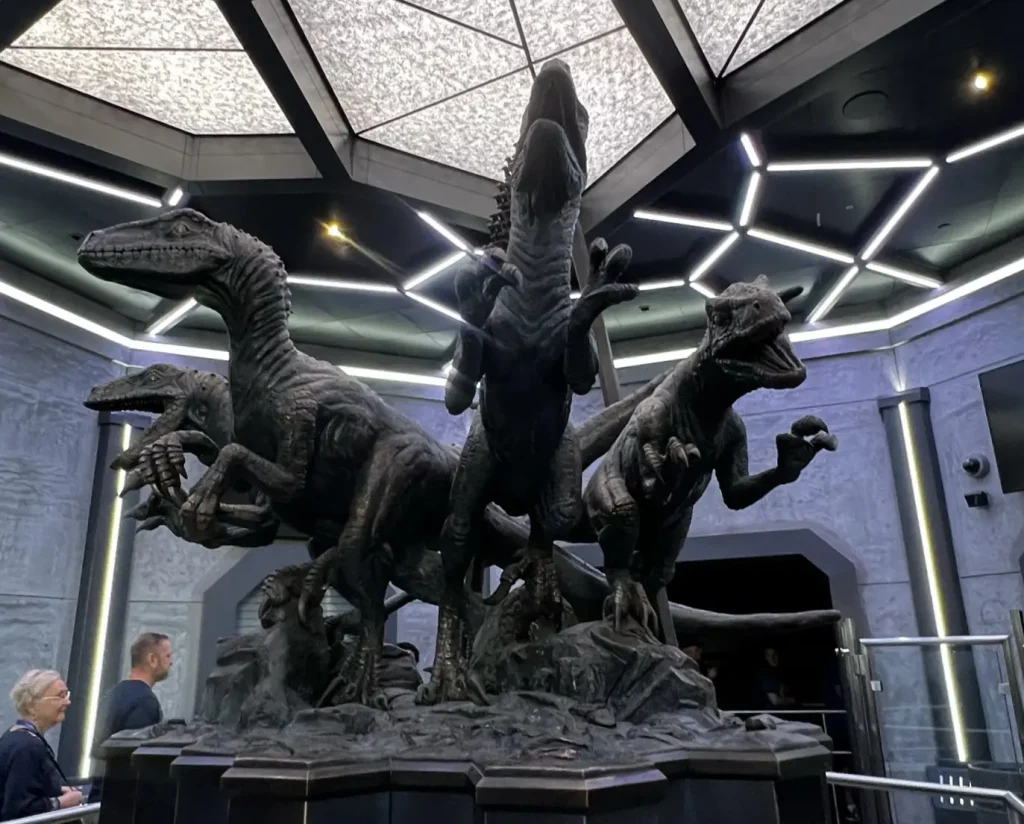 a Large, Dramatic Statue of Three Velociraptors is Displayed Indoors Under a Geometric Skylight at Universal Orlando Resort, with People Standing Nearby and Walls Featuring a Textured, Prehistoric Design. This Spot is a Must-see for Any Attraction Guide. - Favorite Grampy Travels - Favorite Grampy Travels 2026