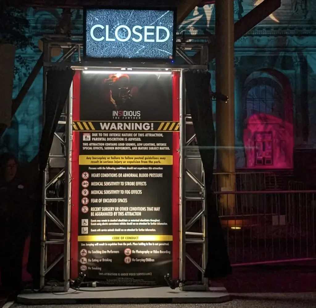 a Haunted House Entrance at Universal Orlando Resort Features a Large "closed" Sign Above a Warning Poster for the “insidious” Attraction, Listing Health Risks and Rules. the Area is Dimly Lit with a Colorful, Eerie Background. - Favorite Grampy Travels - Favorite Grampy Travels 2026