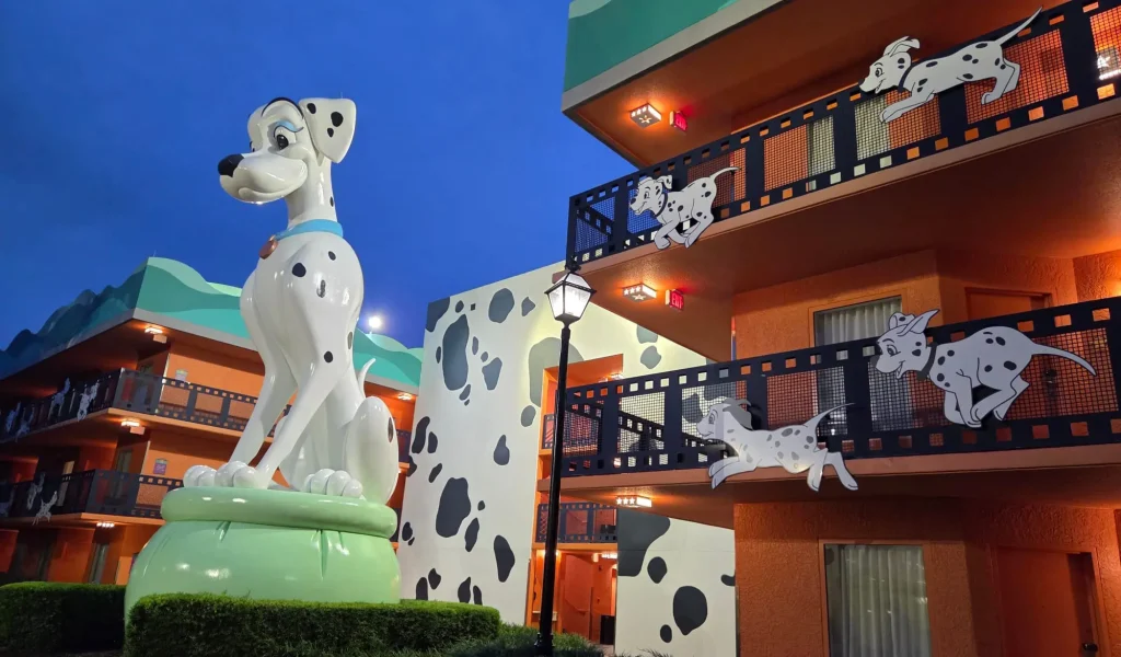A large statue of a Dalmatian dog sits outside a brightly colored building with playful puppy cutouts, inspired by 101 Dalmatians, at one of the fun Walt Disney World Resort Tiers, glowing at dusk. - Favorite Grampy Travels