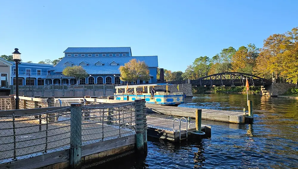Wdw-port-orleans-riverside-resort-ferry-boat - Favorite Grampy Travels a Sunny Waterfront Scene at Walt Disney World, Featuring a Blue-roofed Building, a Dock with Tied Boats, a Small Ramp, and a Wooden Bridge Crossing a Calm River Surrounded by Trees—perfect for Exploring the Charm of Resort Tiers. - Favorite Grampy Travels - Favorite Grampy Travels 2026