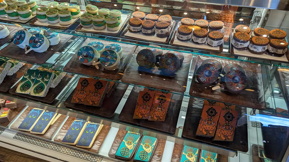 How-to-treat-your-dragon-display-case - Favorite Grampy Travels a Bakery Display Case with Shelves Filled with Intricately Decorated Cookies and Pastries in Various Shapes, Colors, and Patterns, Including Round and Rectangular Designs with Blue, Gold, and Orange Icing. - Favorite Grampy Travels - Favorite Grampy Travels 2026