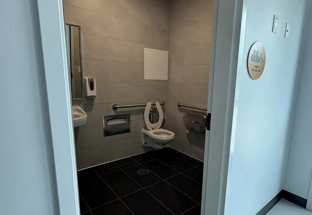 an Accessible Restroom at Universal Kids Resort Features a Wall-mounted Toilet, Grab Bars, a Sink with Mirror, Toilet Paper Dispenser, Soap Dispenser, and Tiled Floor Part of the Resort's Family Services for Guest Comfort. - Favorite Grampy Travels - Favorite Grampy Travels 2026
