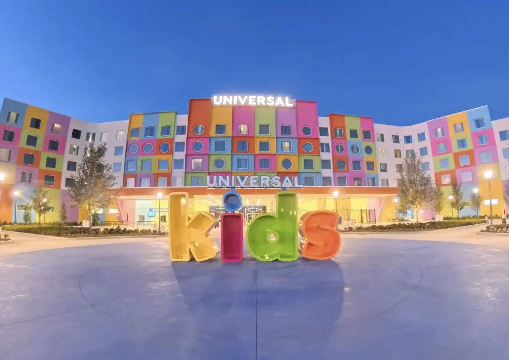 A colorful hotel building with a sign reading UNIVERSAL and large, playful letters spelling kids in front. The vibrant square and circular windows glow at dusk—an inviting scene perfect for your Universal Kids Resort Planning Guide. - Favorite Grampy Travels