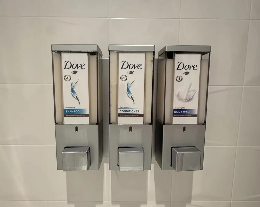 Ukr-hotel-room-dove-soap - Favorite Grampy Travels Three Wall-mounted Dove Dispensers Labeled Shampoo, Conditioner, and Body Wash Are Installed Side by Side on a White Tiled Wall. Each Has a Pump for Dispensing the Product. - Favorite Grampy Travels - Favorite Grampy Travels 2026
