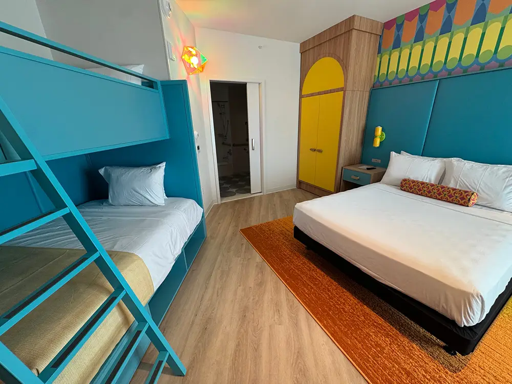 Bedroom with Blue Bunk Bed on the Left and a Large White Bed on the Right, Yellow Wardrobe, and Colorful Mural. - Favorite Grampy Travels 2026 - Favorite Grampy Travels 2026