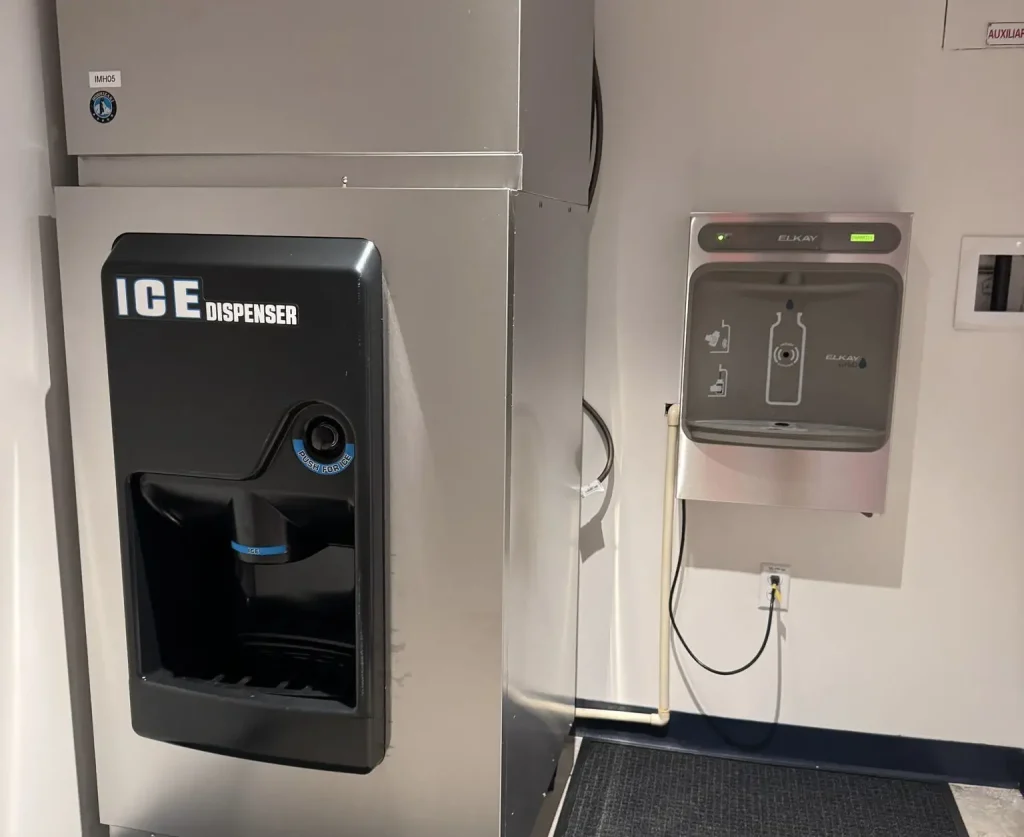 a Stainless Steel Ice Dispenser is on the Left, and a Wall-mounted Filtered Water Bottle Filling Station with a Digital Display is on the Right, Both in a Clean Indoor Setting at Universal Kids Resort Family Services. - Favorite Grampy Travels - Favorite Grampy Travels 2026