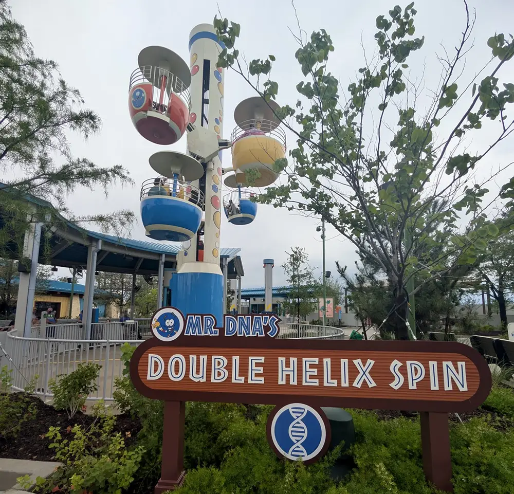 Ukr-jurassic-world-adventure-camp-mr-dnas-double-helix-spin - Favorite Grampy Travels Mr. Dna - Favorite Grampy Travels 2026's Double Helix Spin sign at Universal Kids Resort with the tower ride and coloured gondolas behind it
