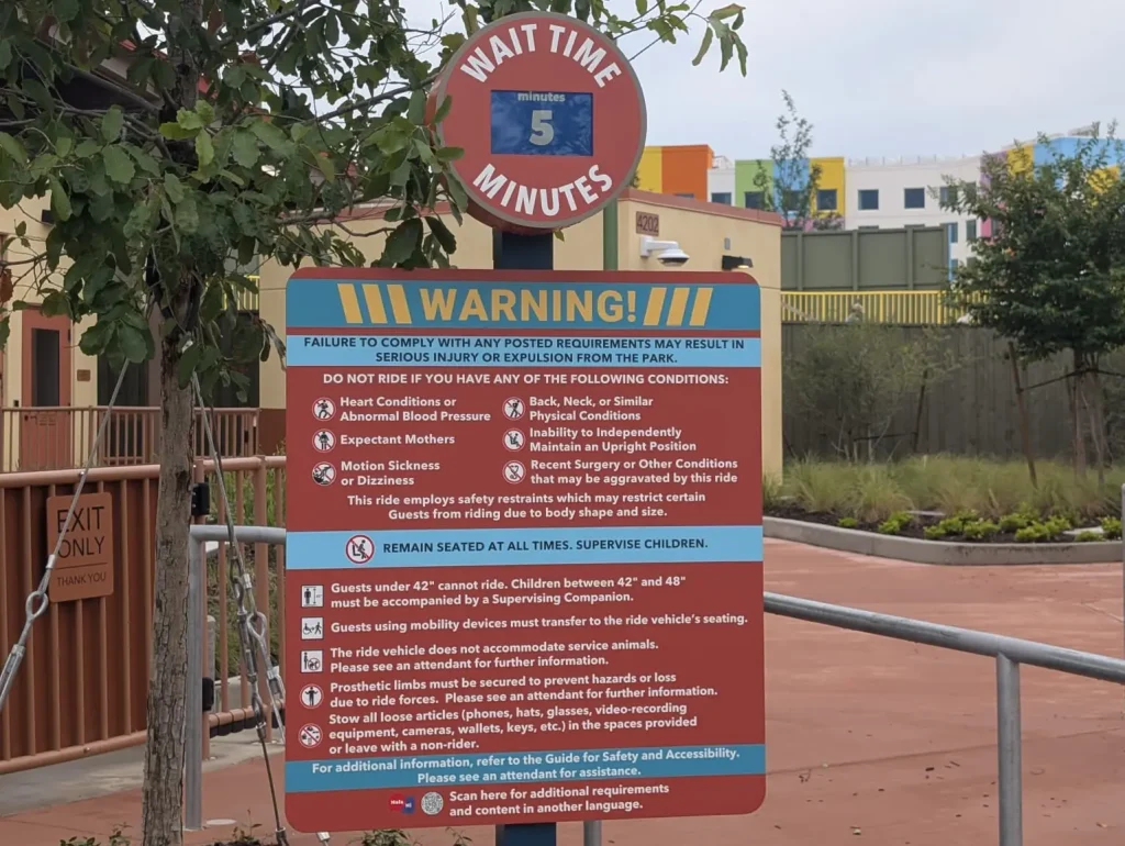 a Theme Park Sign at Universal Kids Resort Shows a 5-minute Wait, Health Warnings, Safety Tips, and Supervision Rules for Children. Buildings and Trees Are Visible in the Background—a Helpful Detail from the Universal Kids Resort Planning Guide. - Favorite Grampy Travels - Favorite Grampy Travels 2026