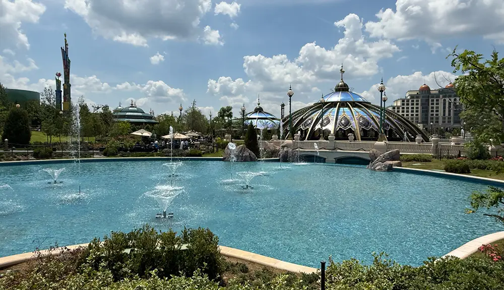 a Large Blue Fountain Pool with Multiple Water Jets, Surrounded by Greenery. in the Background Are Ornate Domed Buildings with Intricate Designs, Under a Partly Cloudy Sky. - Favorite Grampy Travels - Favorite Grampy Travels 2026