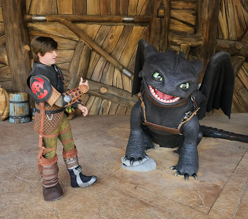 a Person in a Hiccup Costume from How to Train Your Dragon Stands Indoors, Giving a Thumbs Up Next to a Large, Smiling Toothless Dragon Figure. the Background Features Wooden Planks and Medieval Decor. - Favorite Grampy Travels - Favorite Grampy Travels 2026