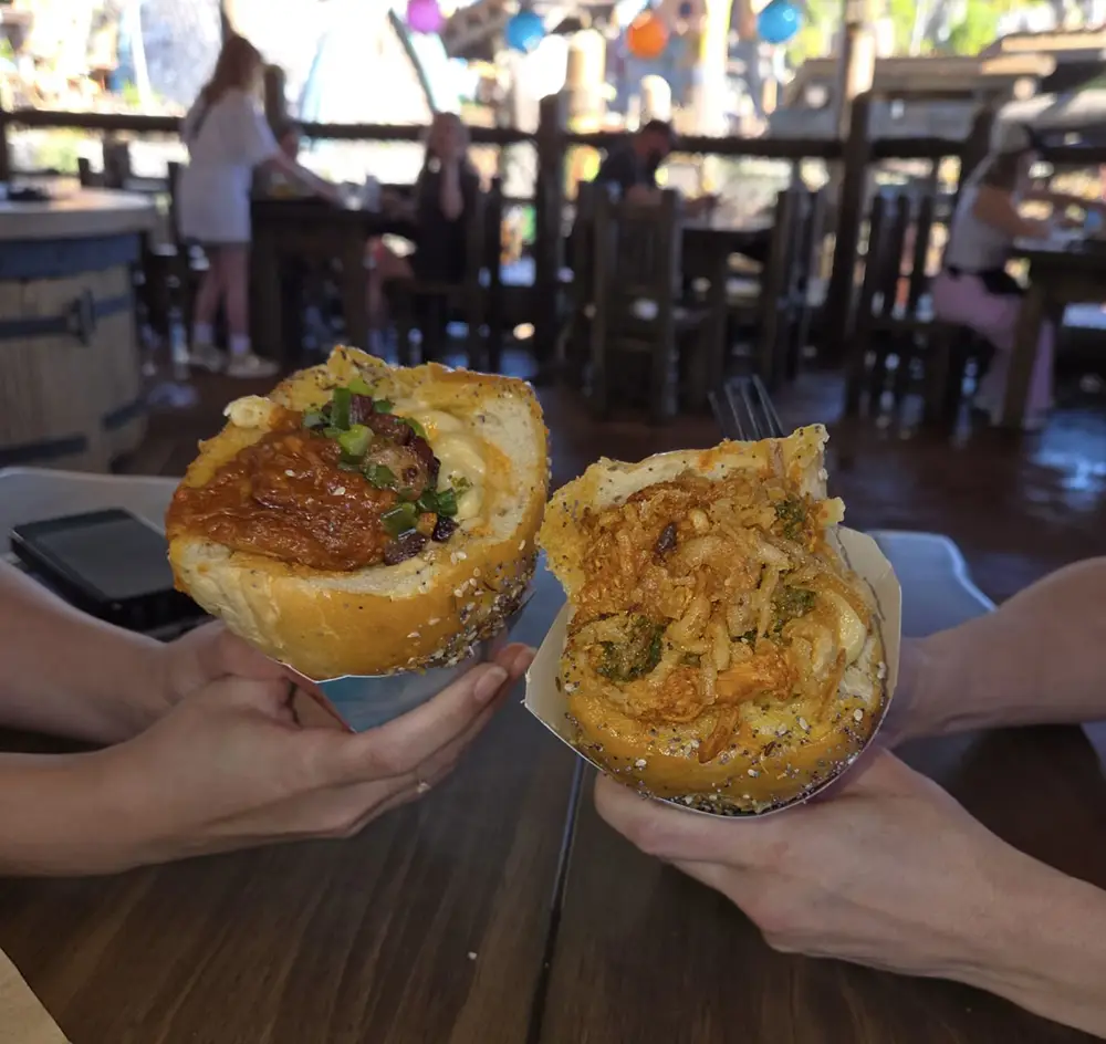 Two Hands Hold Large Sandwich Rolls Filled with Savory Ingredients Like Meat, Sauce, and Vegetables Inside a Lively Isle of Berk Restaurant with Wooden Tables and Colorful Decorations, Showcasing Unique Dining Options in Epic Universe. - Favorite Grampy Travels - Favorite Grampy Travels 2026