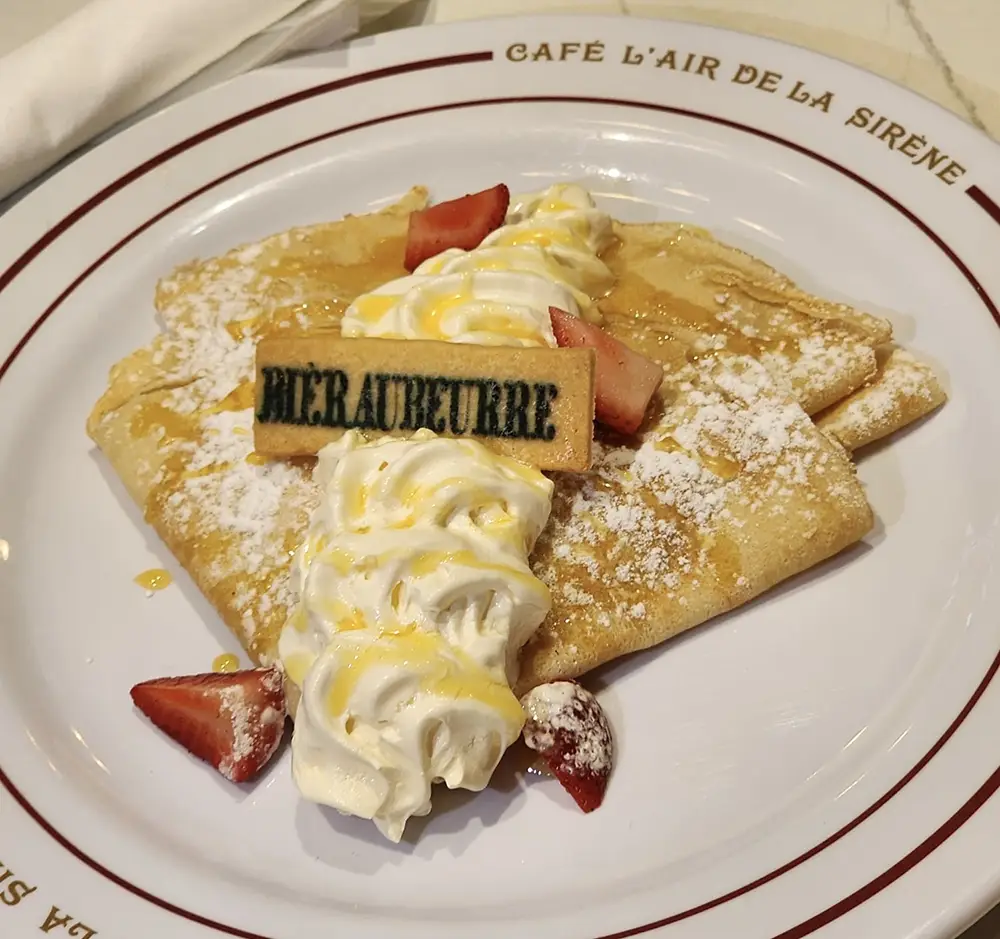 a Plate with Folded Crepes Topped with Whipped Cream, Powdered Sugar, Strawberry Slices, a Rectangular Cookie, and a Drizzle of Sauce—perfect for Dining Like You’re at the Ministry of Magic. the Plate Reads CafÉ Lair De La Sirene on the Rim. - Favorite Grampy Travels - Favorite Grampy Travels 2026