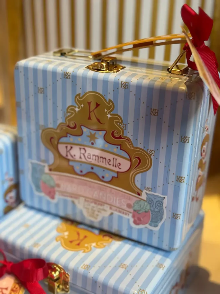 a Decorative Blue and White Striped Tin Box with a Gold Handle, Red Ribbon, and a Label Reading K. Rammelle—perfect for Elegant Dining—stacked with Similar Tins in the Background, Reminiscent of Ministry of Magic Sophistication. - Favorite Grampy Travels - Favorite Grampy Travels 2026