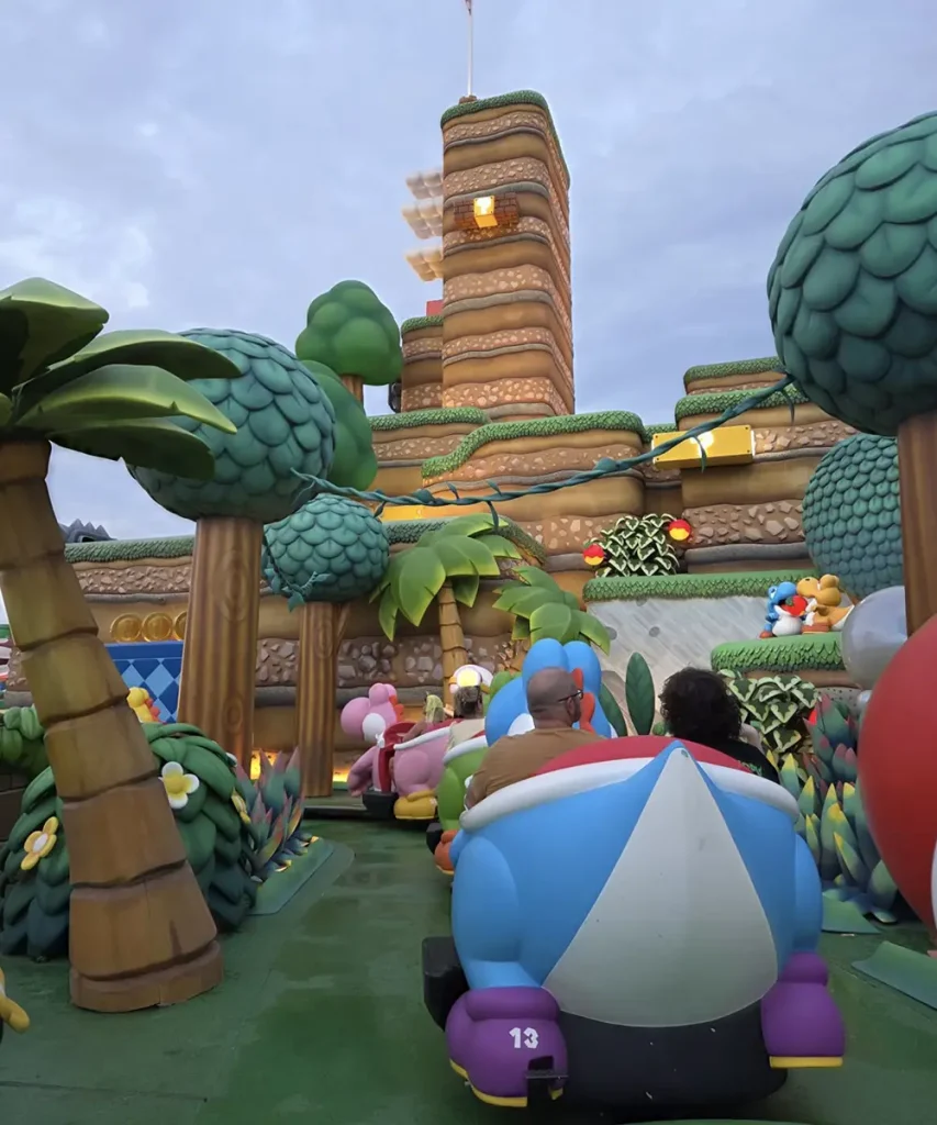 Families and Kids Ride on Colorful Mario Kart-themed Vehicles Through a Vibrant, Cartoon-like Landscape with Palm Trees and a Tall, Layered Mountain, Guided by the Playful Spirit of the Super Mario Video Game Series. - Favorite Grampy Travels - Favorite Grampy Travels 2026