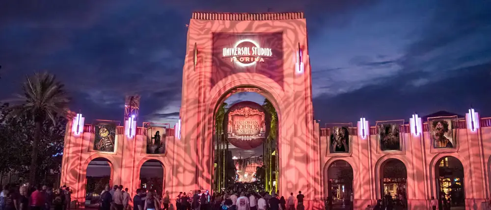 Universal Studios Orlando entrance lit in pink for Halloween Horror Nights, with a crowd gathered at dusk.