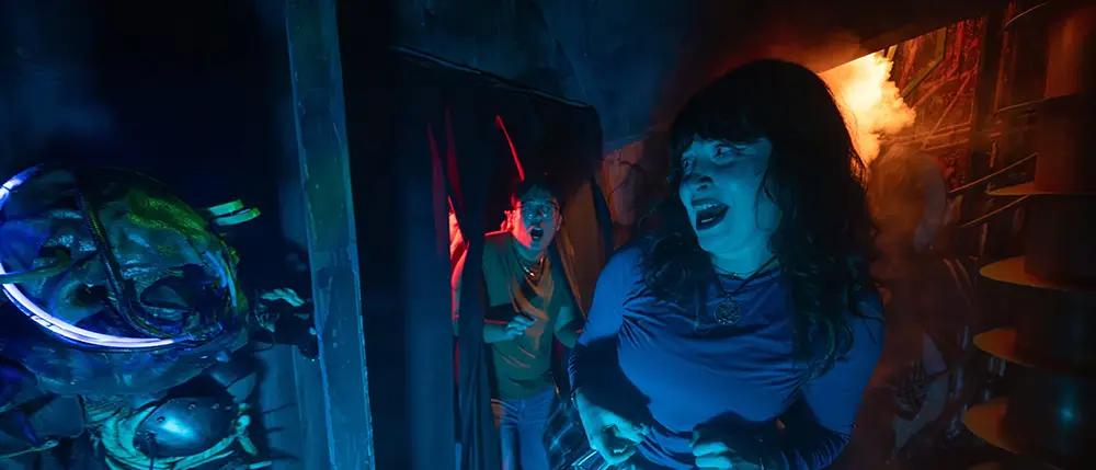 Two People Look Scared As They Move Through a Dark, Eerie Hallway with Blue and Red Lighting, Surrounded by Creepy Props and Smoke Inside a Haunted House at Universal Orlando's Halloween Horror Nights. - Favorite Grampy Travels - Favorite Grampy Travels 2026