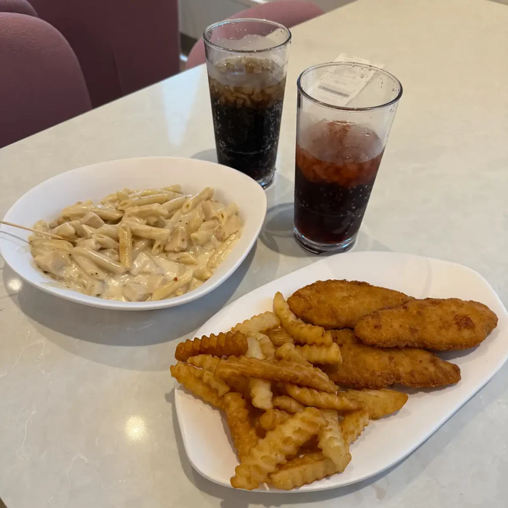 a Table at the Curiosity Cafe at Universal Kids Resort Hotel Features a Bowl of Creamy Penne Pasta, Crinkle-cut Fries, Breaded Chicken Strips on a Plate, and Two Glasses of Soda with Ice. - Favorite Grampy Travels - Favorite Grampy Travels 2026
