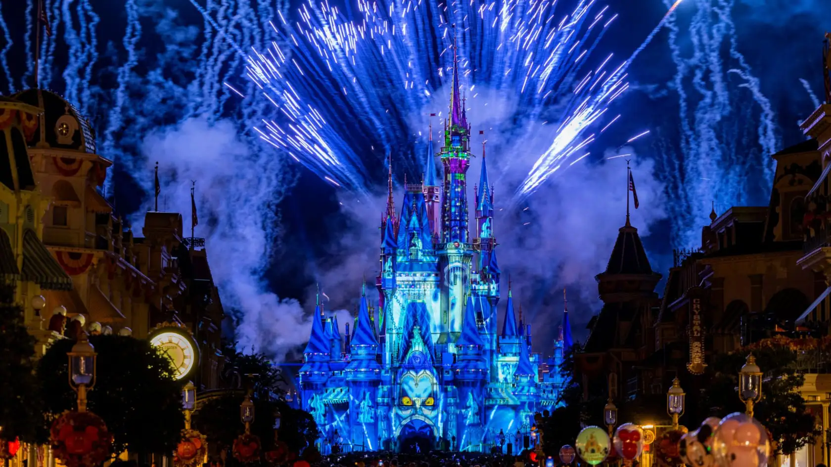 Mickeys Not So Scary Halloween Fireworks Behind Disney Cinderella Castle Illuminated in Blue Lights at Night with Colorful Fireworks Bursting in the Sky Above, Surrounded by Clouds of Smoke and Festive Decorations in the Foreground. - Favorite Grampy Travels - Favorite Grampy Travels 2026 - Favorite Grampy Travels 2026