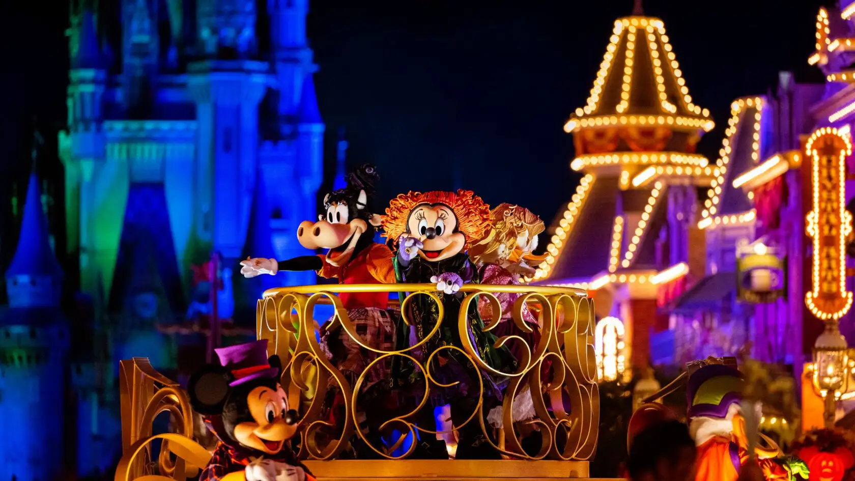 at Mickeys Not So Scary Halloween Party Parade, Disney Characters in Colorful Costumes Wave from a Brightly Lit Parade Float at Night, with Illuminated Castle and Buildings in the Background. - Favorite Grampy Travels - Favorite Grampy Travels 2026 - Favorite Grampy Travels 2026