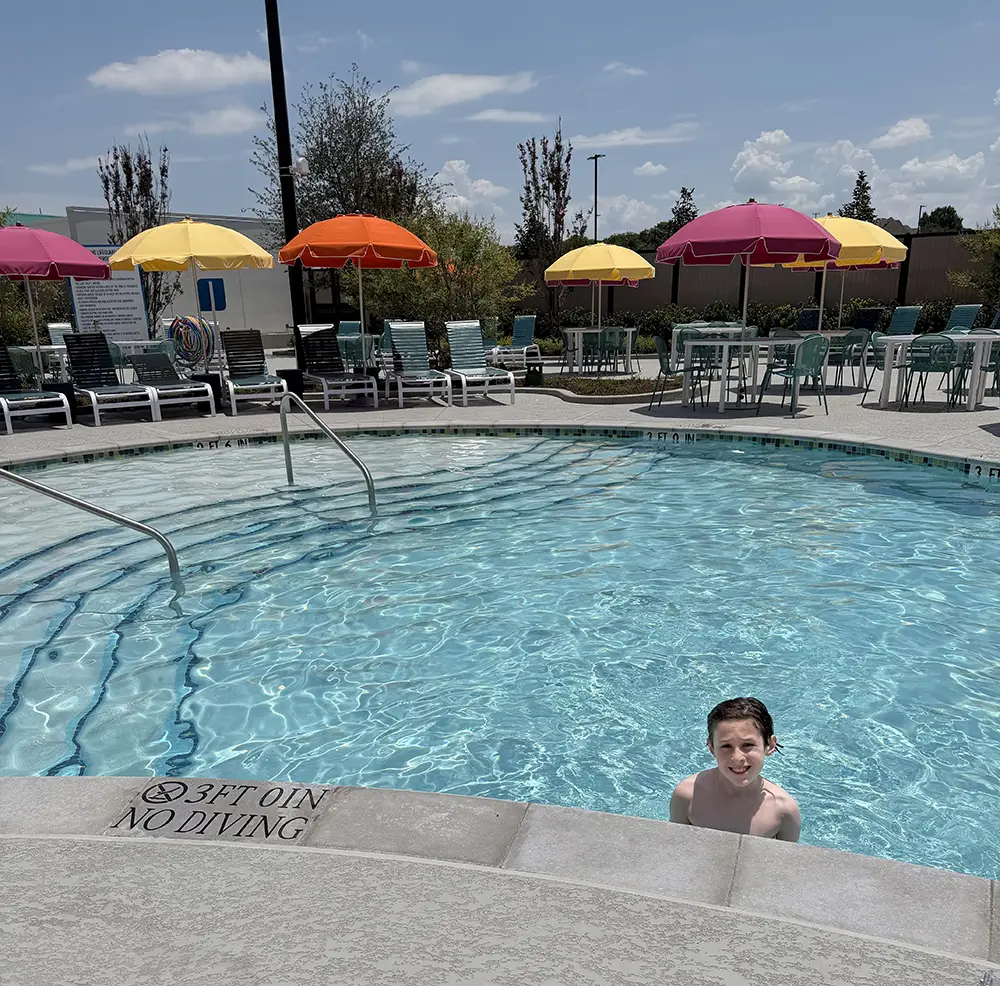 on His First Day at the Universal Kids Resort, a Boy Stands in a Clear Outdoor Pool Near the Edge. Lounge Chairs and Colorful Umbrellas Are Arranged in the Background Under a Sunny Sky, and You Can Almost Hear the Excitement from Nearby Resort Rides. the Pool Depth Sign Reads 3 Ft 0 In, No Diving. - Favorite Grampy Travels - Favorite Grampy Travels 2026