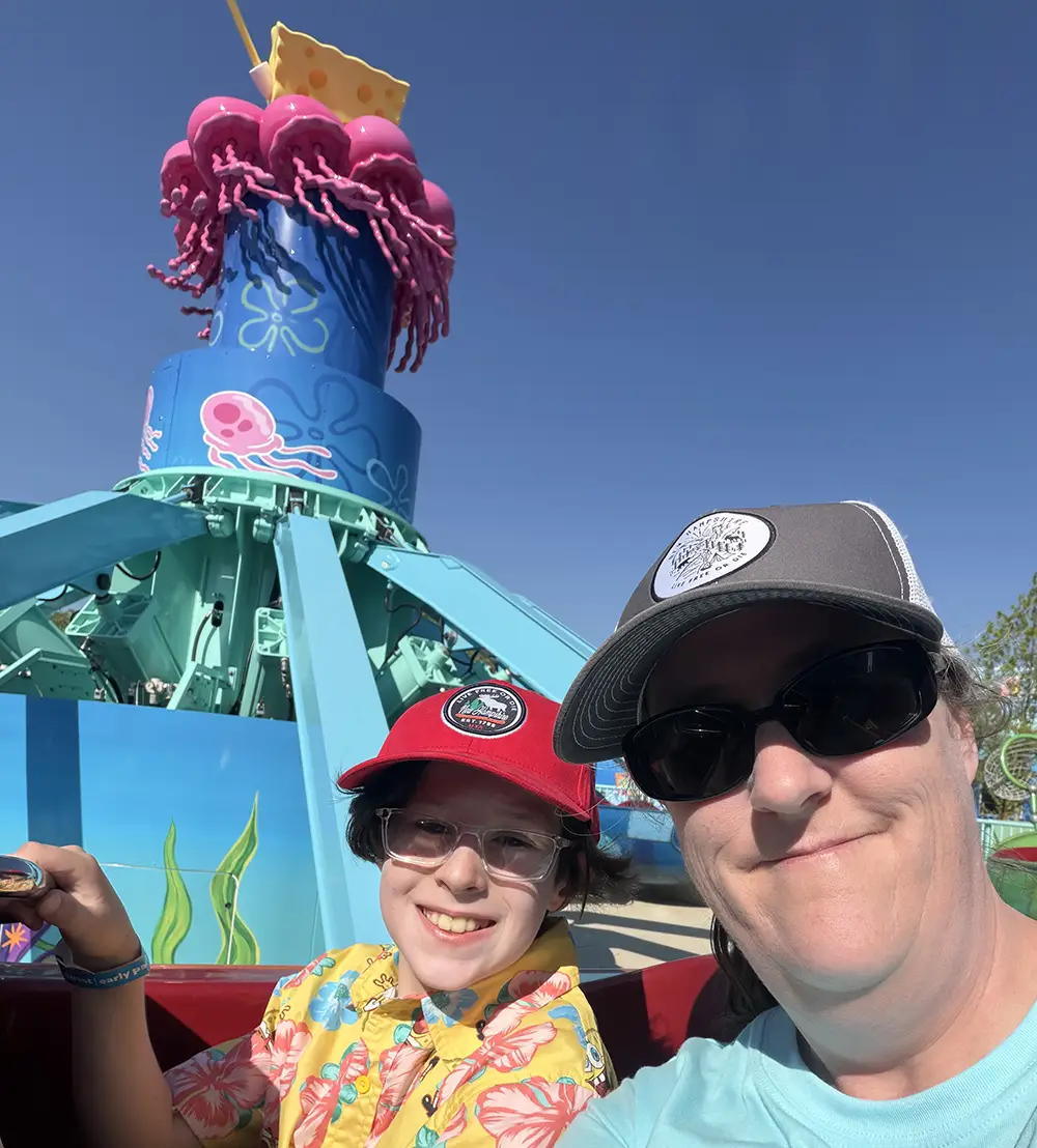 a Child and Adult Smile for a Selfie at an Amusement Park on Their First Day, with a Colorful Jellyfish-themed Ride and a Spongebob Squarepants Figure from the Universal Kids Resort Rides in the Background Under a Clear Blue Sky. - Favorite Grampy Travels - Favorite Grampy Travels 2026