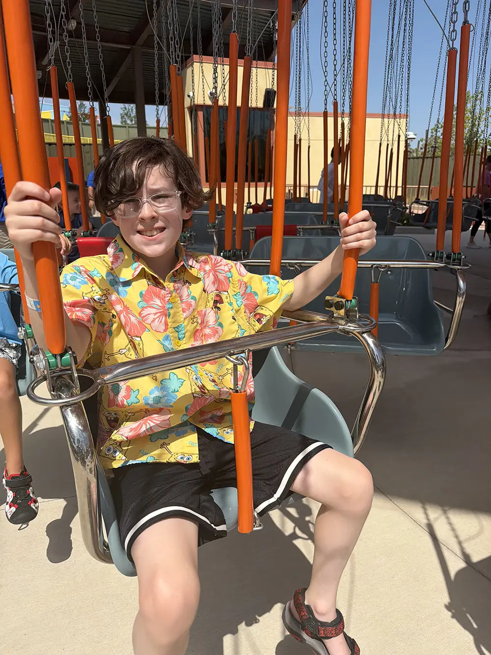 Ukr-swings-over-del-mar - Favorite Grampy Travels Smiling Boy Riding Swings over Del Mar at Universal Kids Resort, Seated on a Swing with Orange Support Poles Under a Clear Sky - Favorite Grampy Travels 2026