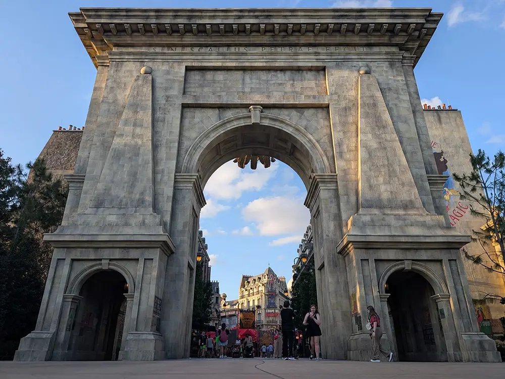 Large Stone Archway with People Walking Underneath, Reminiscent of the Grand Entrances Found in the Wizarding World of Harry Potter; Buildings and Blue Sky with Clouds Are Visible Through the Arch, with Trees on Either Side. - Favorite Grampy Travels - Favorite Grampy Travels 2026