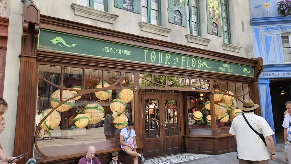 a Storefront with “tour En Floo” Signage, Large Windows Displaying Globe-like Decorations Reminiscent of Magical Artifacts from the Wizarding World of Harry Potter, and People Sitting and Standing Outside, Including One Man in a Hat Facing Away. - Favorite Grampy Travels - Favorite Grampy Travels 2026