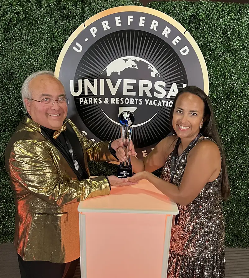 Manny Oliverez and Nikki Hendrix of Favorite Grampy Travels Hold a Trophy for Reaching Universal U-preferred Platinum Agency Status, in Front of a Universal Parks and Resorts Vacations U-preferred Backdrop. - Favorite Grampy Travels 2026 - Favorite Grampy Travels 2026