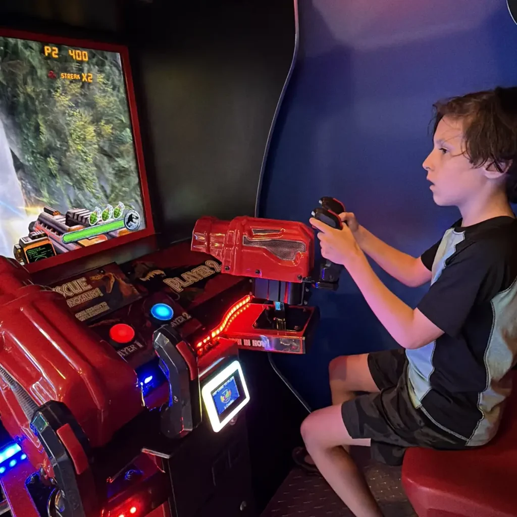 a Boy Sits and Plays an Arcade Shooting Game at the Universal Kids Resort Hotel Arcade, Holding a Red Gun Controller and Focusing on the Large Screen in Front of Him. - Favorite Grampy Travels - Favorite Grampy Travels 2026