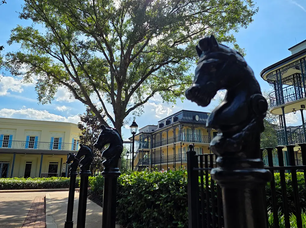Wdw-port-orleans-french-quarter-exterior-horse - Favorite Grampy Travels Decorative Black Knight Chess Pieces Top Fence Posts in Front of Yellow Buildings and Lush Greenery at Disney’s Port Orleans Riverside Resort, with a Large Tree and Blue Sky with Clouds in the Background. - Favorite Grampy Travels - Favorite Grampy Travels 2026