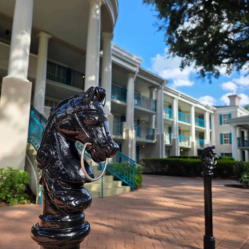 Wdw-port-orleans-riverside-magnolia-bend-exterior-horse - Favorite Grampy Travels a Close-up of a Black Horse-head Hitching Post in Front of a White Building with Columns, Teal Railings, and Balconies Under a Blue Sky with Clouds at Disney - Favorite Grampy Travels 2026's Port Orleans Riverside Resort. - Favorite Grampy Travels