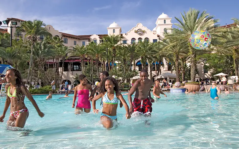 Children Splash and Play in a Large, Sunny Resort Pool Surrounded by Palm Trees, with a the Hard Rock Hotel Building in the Background. a Colorful Beach Ball Floats in the Air. - Favorite Grampy Travels - Favorite Grampy Travels 2026 - Favorite Grampy Travels 2026