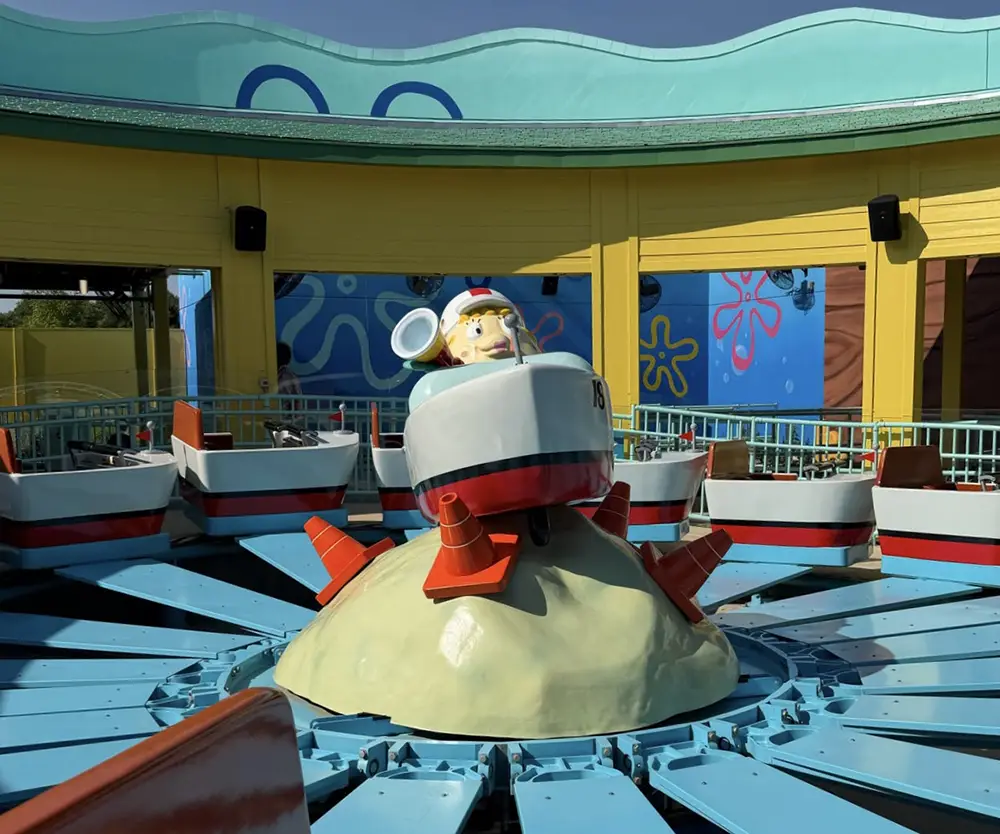 Ukr-spongbob-squarepants-bikini-bottom-mrs-puffs-boating-school - Favorite Grampy Travels A Sandy Cheeks-themed amusement ride with small, sensory-friendly boat seats surrounding a central Sandy Cheeks figure on a sandy mound, set in a colorful, cartoonish area. - Favorite Grampy Travels