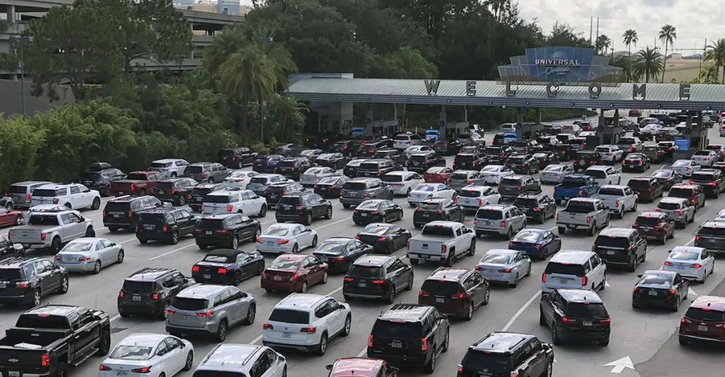 A large traffic jam with many cars waiting at the entrance to Universal Studios, surrounded by trees and palm trees under a cloudy sky. - Favorite Grampy Travels