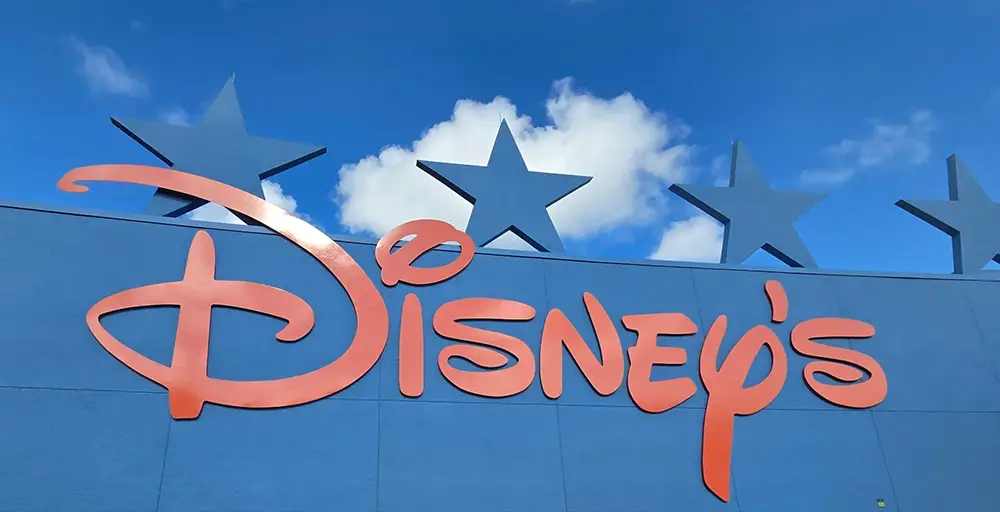 Large, red, stylized Disneys logo on a blue wall with four blue stars and a partly cloudy sky in the background. - Favorite Grampy Travels