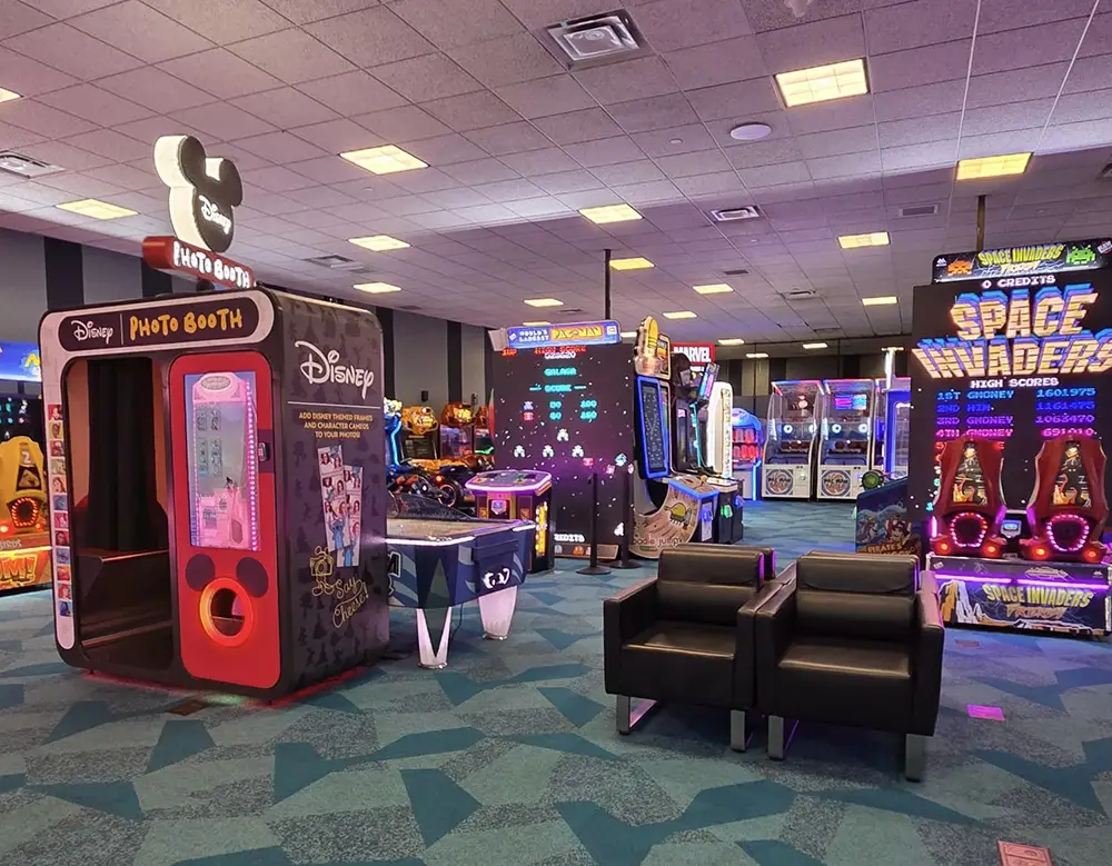 Arcade Room with Various Game Machines, Including a Disney Photo Booth, Air Hockey Table, and Space Invaders Game, Plus Two Black Chairs on a Blue-patterned Carpet. Bright Lights and Colorful Displays Fill the Space. - Favorite Grampy Travels - Favorite Grampy Travels 2026