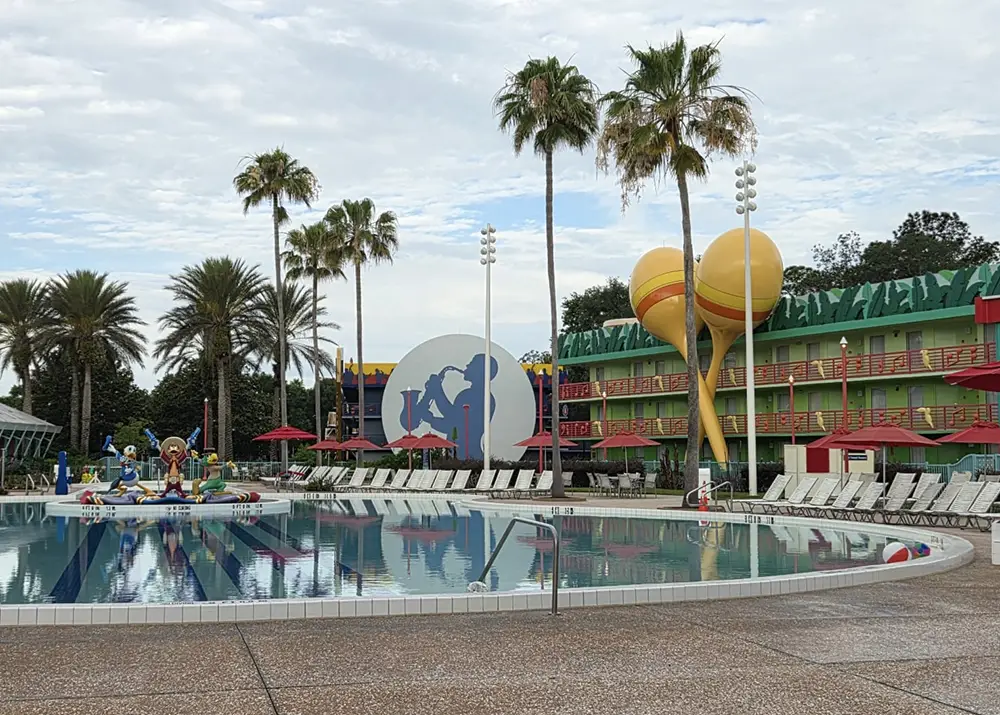 a Hotel Pool Area with Palm Trees, Red Umbrellas, and Large Colorful Decorations, Including Giant Maracas and a Cowboy Silhouette on a Building in the Background. Lounge Chairs Line the Poolside. - Favorite Grampy Travels - Favorite Grampy Travels 2026
